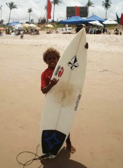 A young surfer in a red rash vest holding a surfboard on the beach at a competition